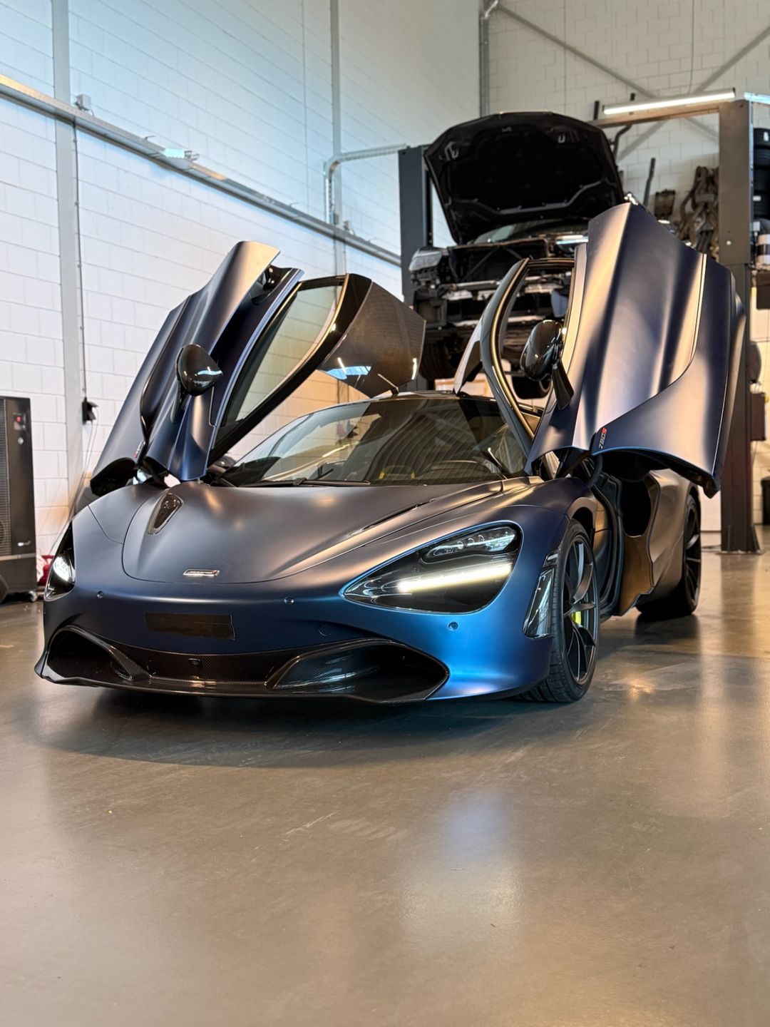McLaren met matblauwe wrap en geopende vlinderdeuren in de werkplaats