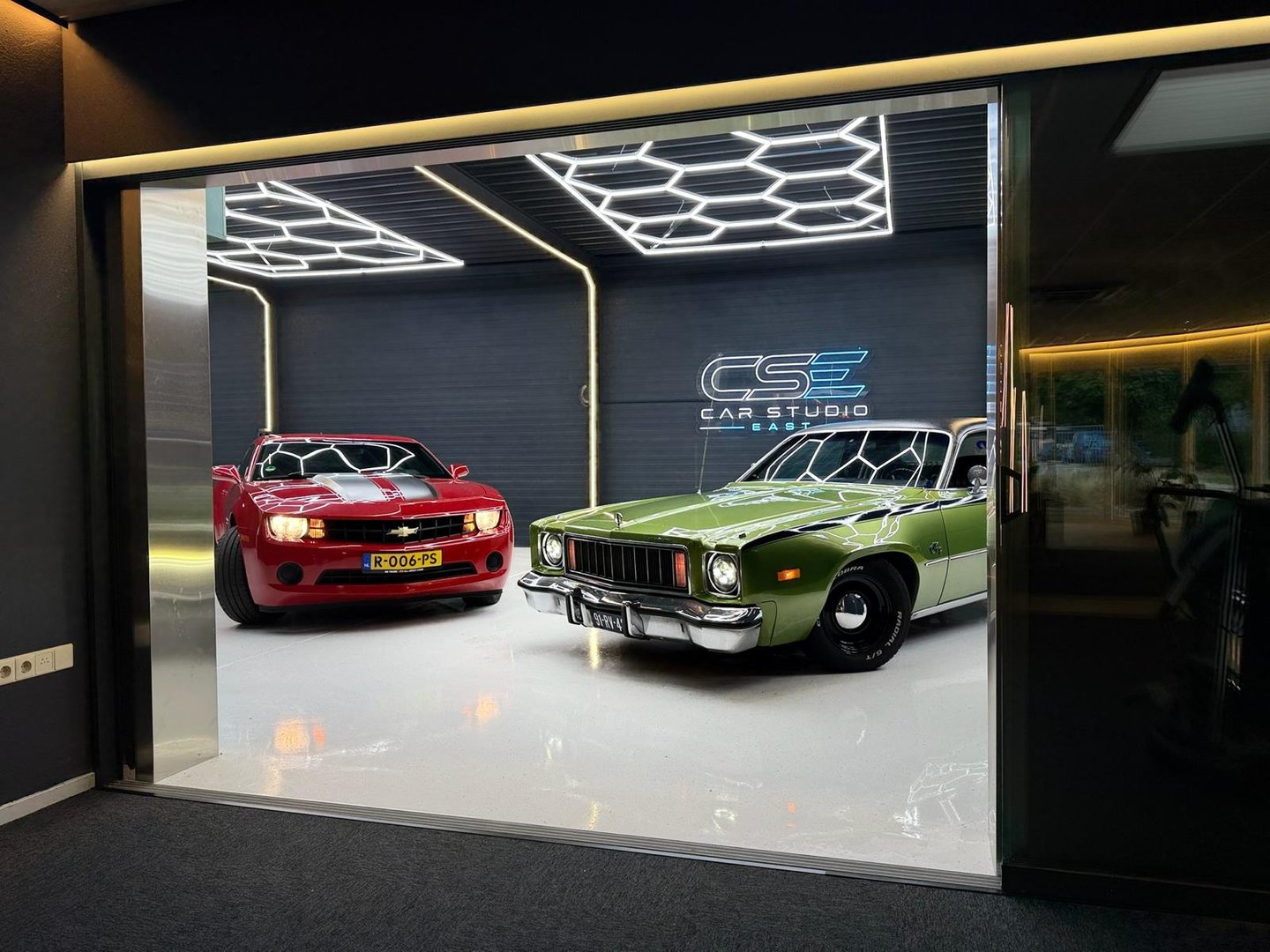 Showroom van Car Studio East met auto's onder de hexagonverlichting en het CSE-logo op de wand